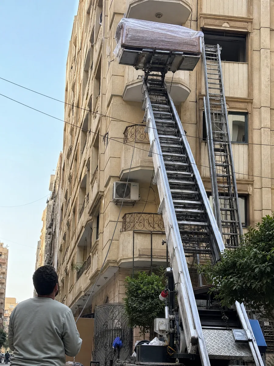 ونش رفع أثاث يرفع كنبة مغلفة إلى بلكونة عمارة في جسر السويس